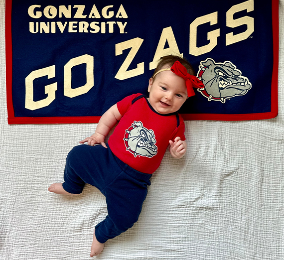 Baby asleep with a tennis ball with a Zag logo on it.